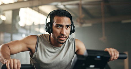 Image showing Asian man, headphones and cycling at gym on machine and listening to music in sports workout or exercise. Serious male person or athlete training on bicycle machine or equipment for healthy cardio
