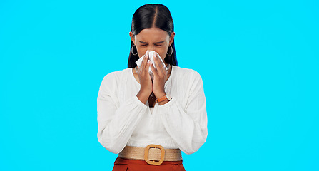 Image showing Woman, blowing nose and sick with tissue in studio for allergies, dust or pollen by blue background. Girl, sneeze and toilet paper with pain, virus and cold for healthcare, wellness and flu symptoms