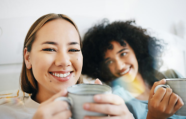 Image showing Coffee, smile and portrait of lesbian couple on bed in conversation for bond and relax together. Happy, rest and interracial lgbtq women laughing, talking and drinking latte in bedroom of apartment.