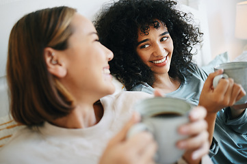 Image showing Coffee, happy and lesbian couple on bed in conversation for bonding and relaxing together. Smile, rest and interracial lgbtq women laughing, talking and drinking latte in bedroom of modern apartment.