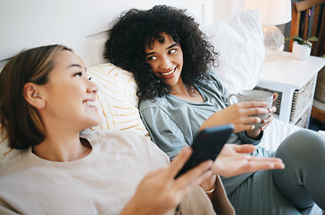 Image showing Phone, coffee and lesbian couple on bed in conversation for bonding, relaxing and resting together. Happy, communication and young lgbtq women networking on cellphone with latte in bedroom at home.