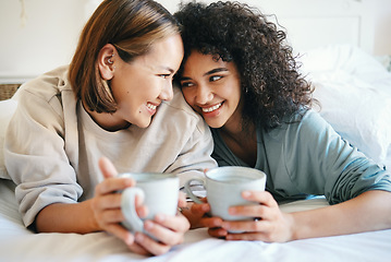 Image showing Coffee, love and lesbian couple on bed in conversation for bonding and relaxing together. Happy, rest and interracial lgbtq women laughing, talking and drinking latte in bedroom of modern apartment.