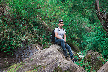 Image showing Man traveler with backpack sitting on rock in the forest.