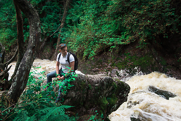 Image showing Man traveler with backpack sitting on rock in the forest.