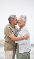 Image showing Senior couple, kiss or hug on beach with smile, embrace and enjoying for retirement, happy or love. Senior citizen, romance and lovers with bond, happiness and vacation for travel, anniversary or fun