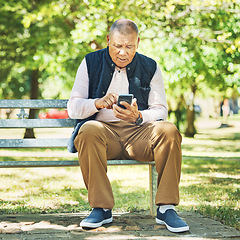 Image showing Senior man, typing and phone on park bench, learning and network with technology online, nature and outdoor. Elderly person, message and email on smartphone, digital and contact in retirement