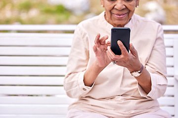 Image showing Senior woman, phone and park outdoor with social media scroll and text sitting on a garden bench. Hands, elderly female person and smile from mobile networking, internet app and online reading