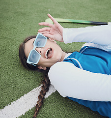 Image showing Woman, hockey and laying on field, break and closeup of sunglasses, pose and relax for practice, training and workout. Happy athlete, playful and excited for exercise, fashion and accessories for fun