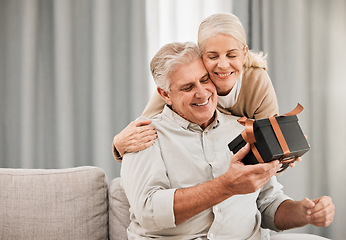 Image showing Happy couple, together and love with gift at home in embrace for birthday, anniversary or event. Mature, man and woman in living room, celebration and bond in happiness with hug, smile and special