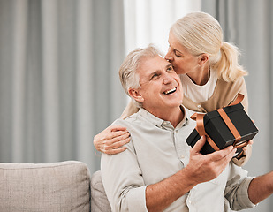 Image showing Old couple, gift and birthday, kiss with love and surprise, man and woman at home, celebration and care. Happiness, present for anniversary with smile for special event and marriage with partner