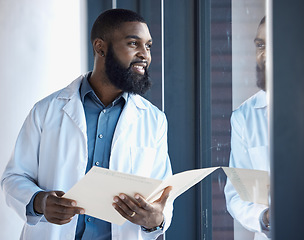 Image showing Doctor, black man and thinking of healthcare information, paperwork or documents by window in building with smile. Person, professional or person thoughtful of notes or charts on paper with ideas