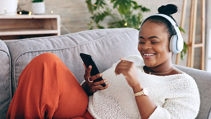 Image showing Black woman on couch, headphones for music and smartphone, relax at home and audio streaming with smile. Happiness, mobile app and using phone for radio or podcast, scroll with technology in lounge