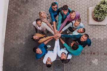 Image showing Top view photo of a group of business people and colleagues standing together holding hands, looking towards the camera, symbolizing unity and teamwork.