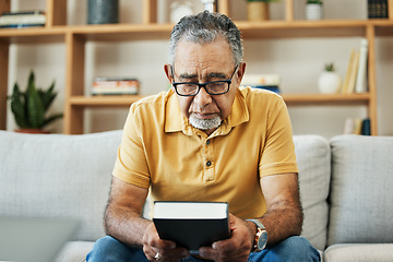 Image showing Mature, man and bible by thinking in home, alone and sadness of memory in living room of thoughts. Elderly, person or grandfather on sofa with hand, holding and book for religion, church or practice