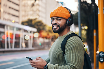 Image showing Phone, headphones and portrait of man in city outdoor, listen to audio or radio sound on internet to travel. Face, streaming music and happy student typing in street on social media in South Africa