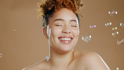 Image showing Woman, bubbles and skincare for beauty, happy with natural cosmetics and glow isolated on brown background. Dermatology, wellness for skin and liquid soap with self care and anti aging in studio