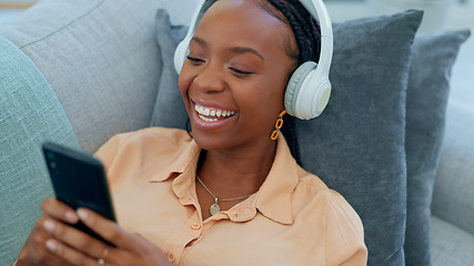 Image showing Happy black woman, headphones and relax with phone on sofa for funny joke in living room at home. African female person smile on mobile app and laughing for social media, meme or entertainment