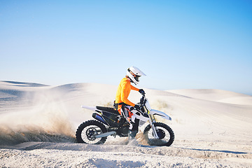 Image showing Extreme sport, motorcycle and athlete with sand by wheels with pride, skill and adrenaline rush. Biker, sunshine and dust with blue sky in fun, fitness and achievement in speed, race and lens flare