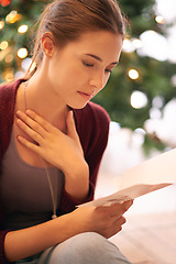 Image showing Young woman reading christmas card, letter and emotional note in home living room during winter celebration, holidays and break. Female, festive message and xmas greeting card, wishes and kindness