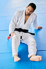 Image showing Sports, injury and pain in legs on karate fitness dojo floor for tournament, training or workout. Professional athlete uniform of martial arts man with knee pain or arthritis at sport club.