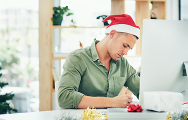 Image showing Christmas, computer and businessman writing at a desk, thinking and planning in his office alone. Festive, season and employee working to meet deadline on xmas eve, write list, note or reminder