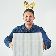 Image showing Christmas, present and celebration with a festive man in studio on a gray background in the holiday season. Tradition, gift and giving with a cheerful male wearing reindeer horns on his head