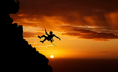 Image showing Sunset sky abseiling, mountain silhouette and hiking man hanging on shadow rope. Fitness risk, adventure freedom challenge and strong, surreal nature adrenaline and cliff climbing on orange landscape