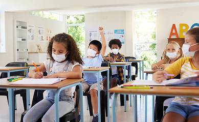 Image showing Young kids learning in classroom after covid pandemic, wearing protective face masks. Little children sitting in school with raised arm to ask questions and studying for their education