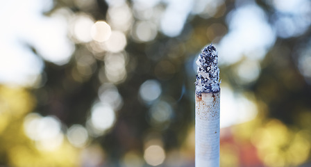 Image showing Cigarette, nicotine and tobacco with a smoking stick burning outdoor on a blurred background with mockup. Smoke, addiction and habit with a smoker lifestyle and the risk or danger of cancer