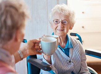 Image showing Senior woman, happy friends and toast coffee in wheelchair in room, house or nursing home together. Elderly women, mug and smile for love, bonding and care in home with disability with happiness