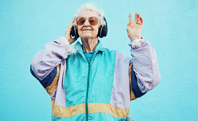 Image showing Happy, elderly and woman with headphone music for wellness, fun and retirement leisure. Urban, retro and funky senior person listening to feel good streaming on headphones at blue wall.