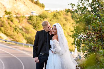 Image showing Happy newlyweds are hugging against the backdrop of a beautiful mountain landscape, the girl looked into the frame with a wide smile