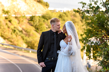 Image showing Happy newlyweds kiss against the backdrop of a beautiful mountain landscape, the girl and the guy look at each other