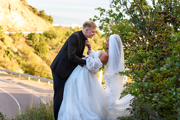 Image showing Happy newlyweds kiss against the backdrop of a beautiful mountain landscape, the girl holds the guy by the tie