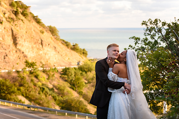 Image showing Happy newlyweds kiss against the backdrop of a beautiful mountain landscape, a girl kisses a guy