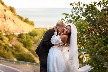 Image showing Happy newlyweds kiss against the backdrop of a beautiful mountain landscape, the girl fervently turns away from the guy