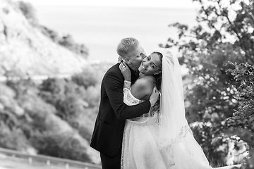 Image showing Happy newlyweds kiss passionately against the backdrop of a beautiful mountain landscape, black and white version