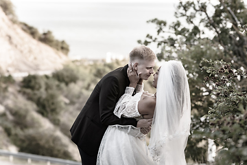 Image showing Happy newlyweds kiss against the backdrop of a beautiful mountain landscape, sepia