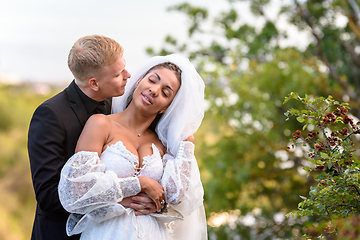 Image showing Happy newlyweds hug against the backdrop of a beautiful mountain landscape, the guy kisses the girl who has closed her eyes