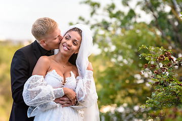 Image showing Happy newlyweds hug against the backdrop of a beautiful mountain landscape, the guy kisses the girl