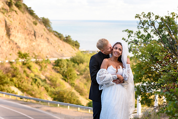 Image showing Newlyweds hugging against the backdrop of a beautiful mountain landscape, the guy kisses the girl