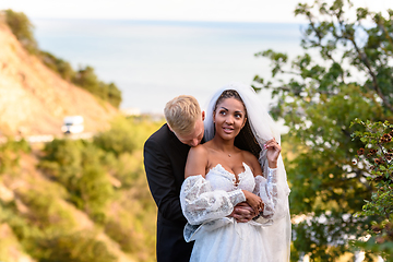 Image showing Newlyweds hug against the backdrop of a beautiful landscape, the guy kisses the shoulder of the girl who shyly looks up