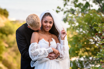 Image showing Newlyweds hug against the backdrop of a beautiful landscape, the guy kisses the neck of the girl who is looking into the frame