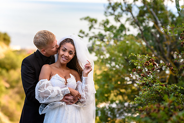 Image showing Newlyweds hug against the backdrop of a beautiful landscape, the guy kisses the girl who is looking into the frame