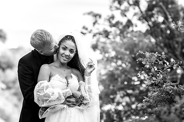 Image showing Happy newlyweds hug against the backdrop of a beautiful mountain landscape, the guy kisses the girl, the girl looks into the frame, black and white version