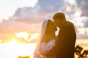 Image showing Happy newlyweds hugging against the backdrop of a cloudy sky in the rays of the setting sun