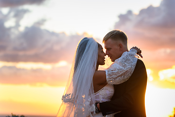 Image showing Happy newlyweds hugging against the sky in the rays of the setting sun