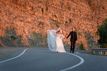 Image showing Happy newlyweds running along a mountain asphalt road