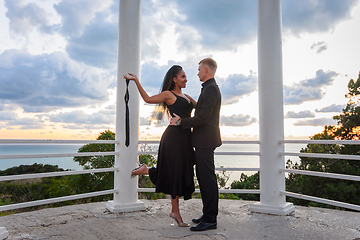 Image showing A young couple in a gazebo against the backdrop of a beautiful landscape, the girl holds the guy's tie