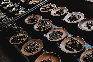 Image showing Various spices displaied on small ceramic and metal plates on black wooden background.